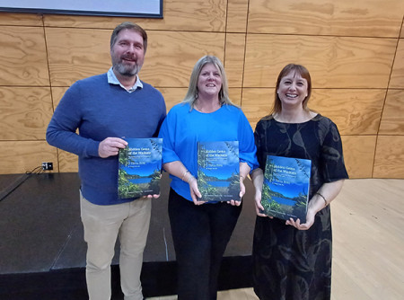 Image of three people standing next to each other holding a book